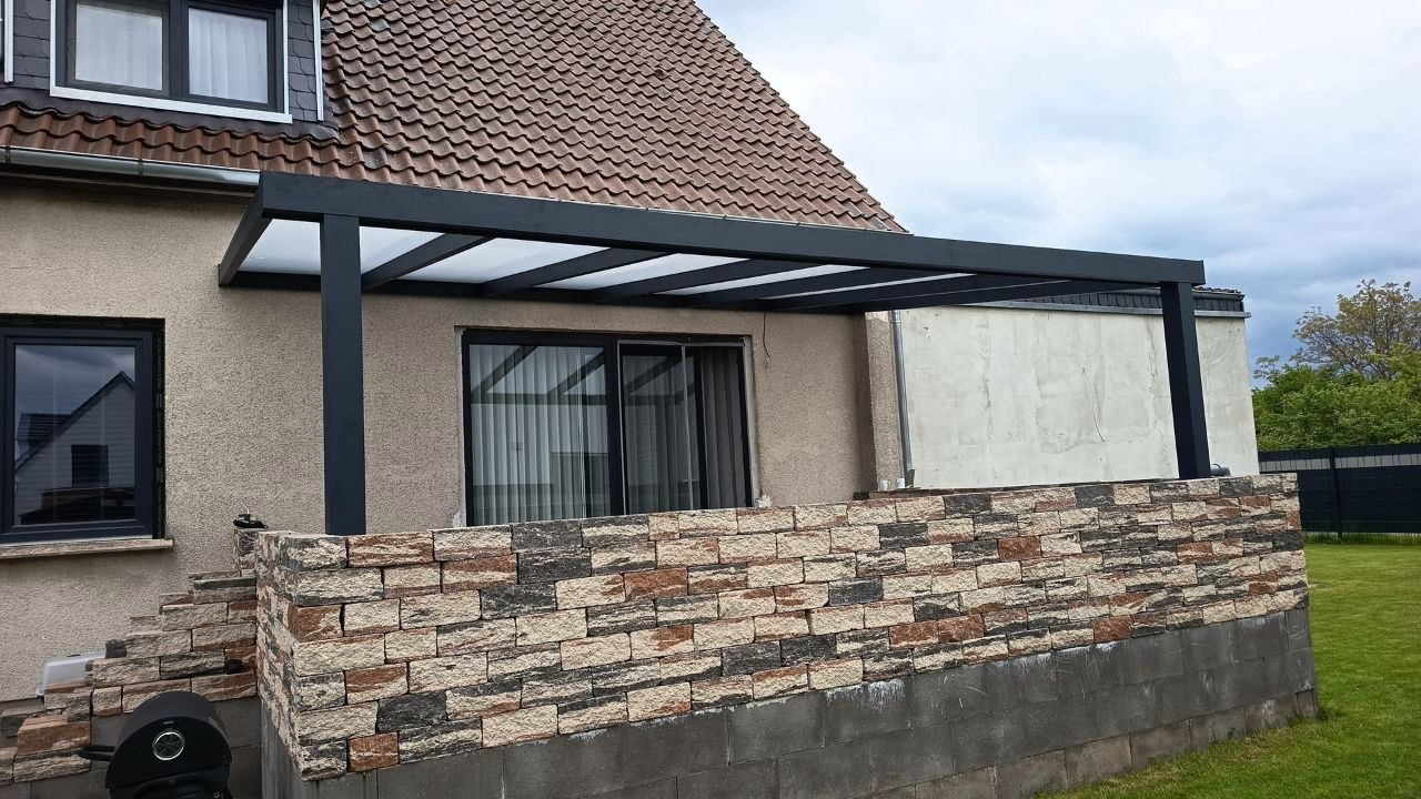 Alu-Terrassenüberdachung als Wandmontage über einer Natursteinmauer