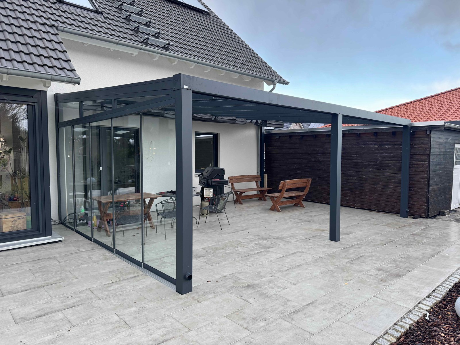 Alu-Terrassenüberdachung in Anthrazit mit Glasschiebewand und Unterdachmarkise an einem Einfamilienhaus