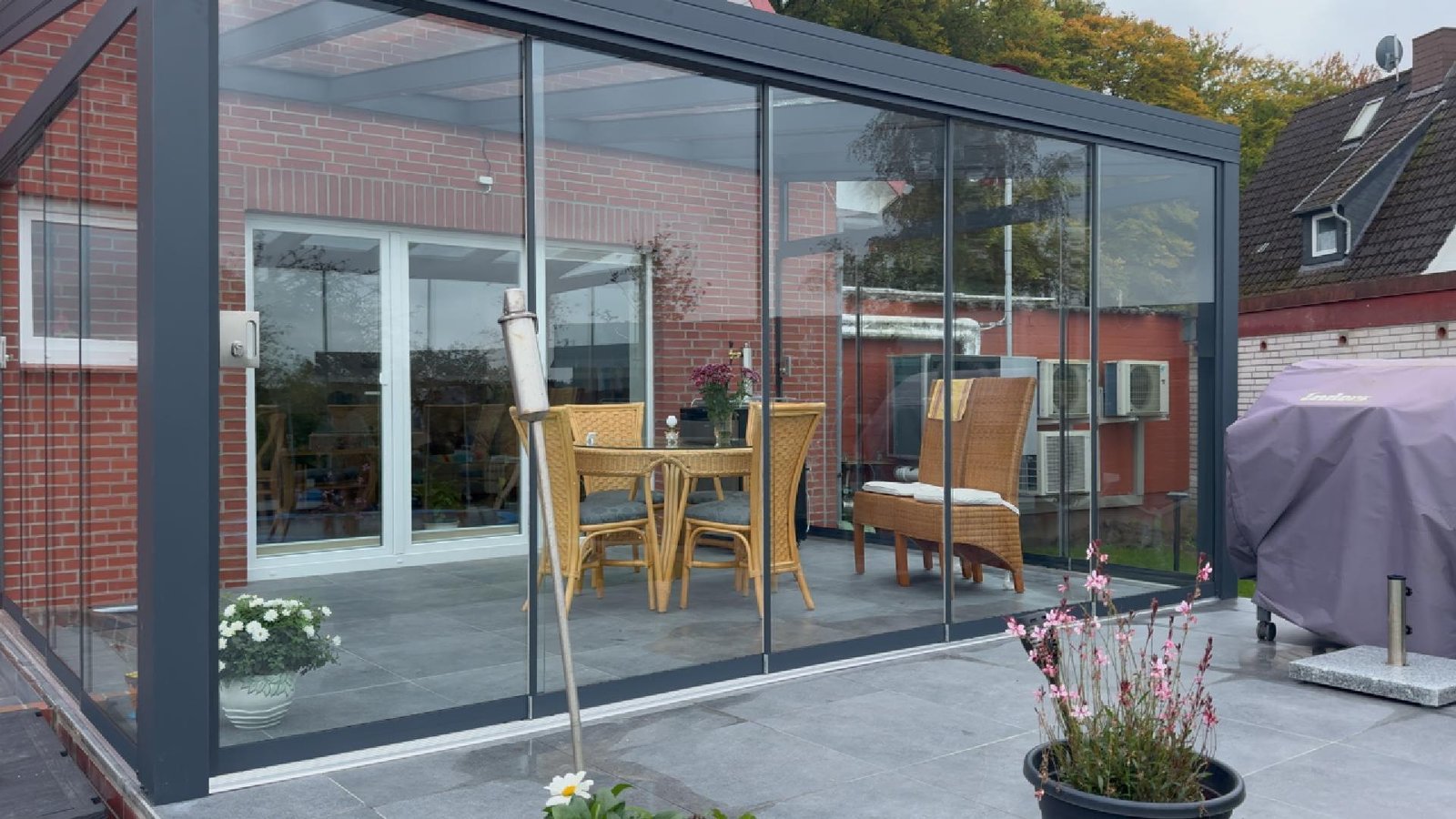 Alu-Terrassenüberdachung mit umlaufender Glasschiebewand an einem Klinkerhaus